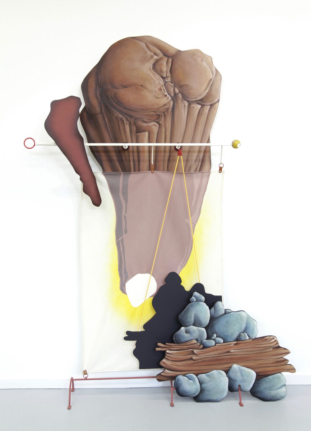 Large mixed media sculpture that is mounted on a white gallery wall, with elements that are on the floor. A large shaped wood panel is painted in trompe l'oeil style to look like brown rock forms; this is the top of the sculpture. A white metal bar is mounted in front of that, while a fabric panel hangs below. A brown metal bar with legs sits on the floor. The lower right of the sculpture is another trompe l'oeil painted wood panel that depicts grey rocks and brown wood.