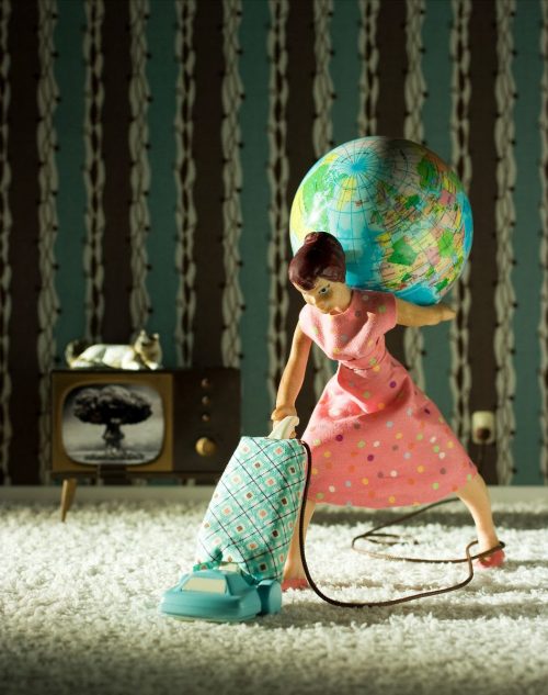 Figurine of a woman vacuuming and holding a globe on her back. The TV in the background shows an atomic bomb exploding.