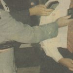 A video still of Untitled (Saturday, October 16, 1993) shows a weathered newspaper clipping of a figure dressed in a white shirt with red tie standing before microphones. Arms reach out from the left side of the shot with tape recorders and additional microphones preparing to record the speaker’s voice.