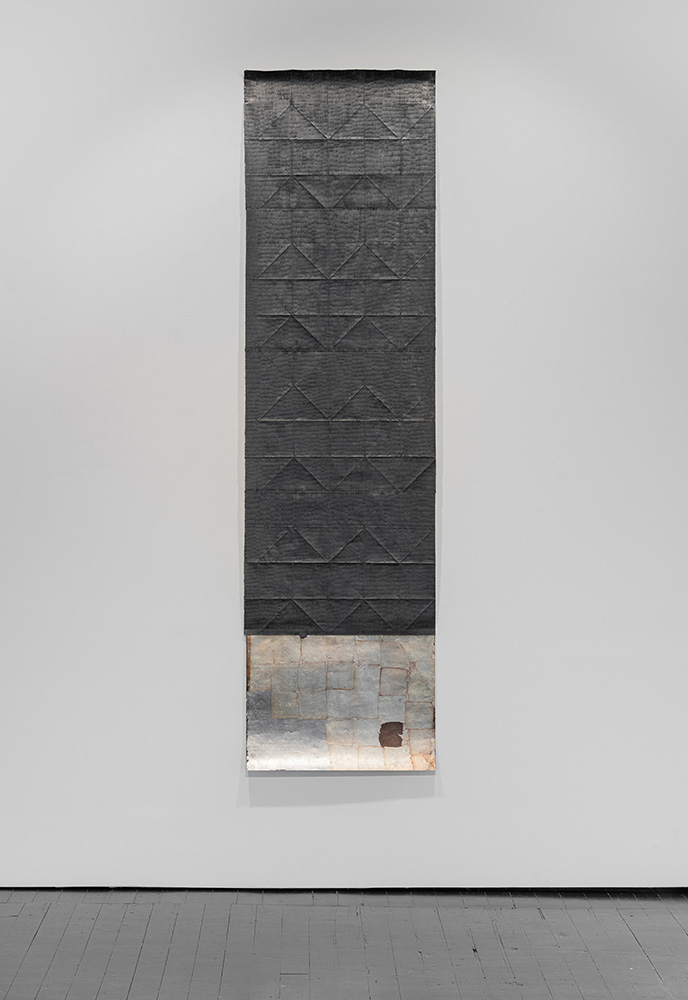 Jenene Nagy artork of vertical dark gray paper with a triangular texture hanging in a gallery