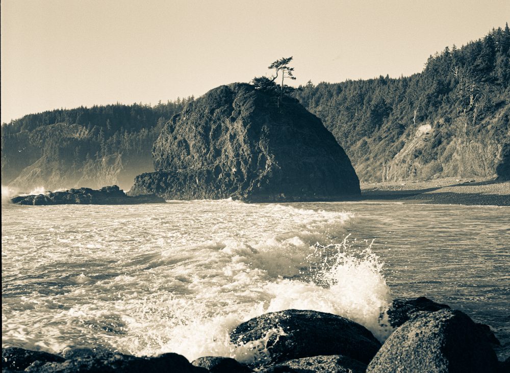 Beach view with a wave crashing. Sea stack in focus in midframe