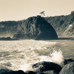 Beach view with a wave crashing. Sea stack in focus in midframe