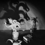 A painting in black and white of a candle and a box of matches in the foreground, two shadow puppets of a dragon and a knight in the mid-ground, and larger cast shadows of the puppets in the background.