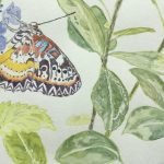 A brightly colored butterfly is perched on a stem with a small blue flower. There are a few stems with green leaves to the right.