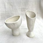 Two small white ceramic vases reminiscent of bird's nest mushroom spores.