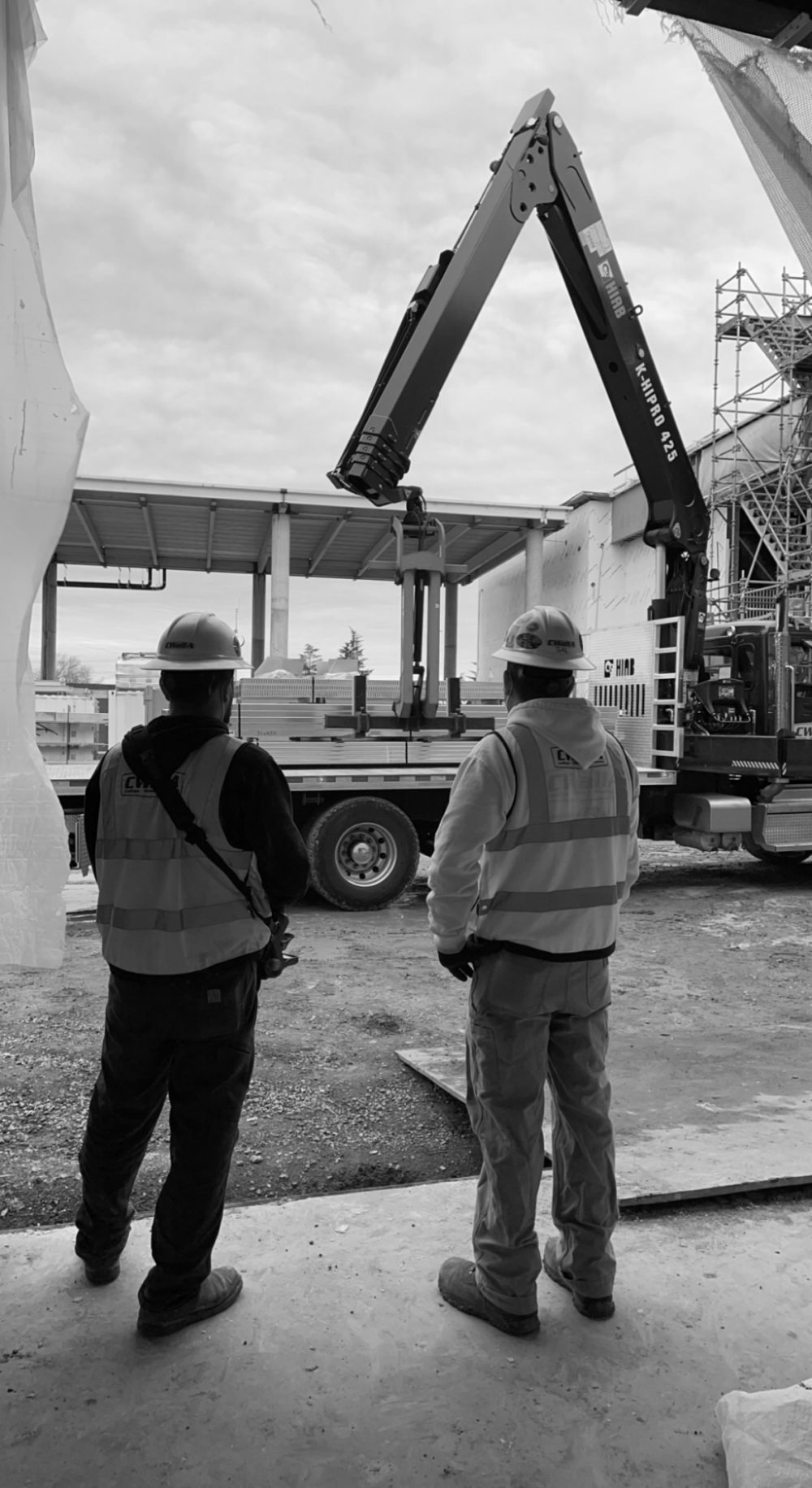 Black and white photograph of two men standing in front of a boom truck.