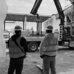 Black and white photograph of two men standing in front of a boom truck.