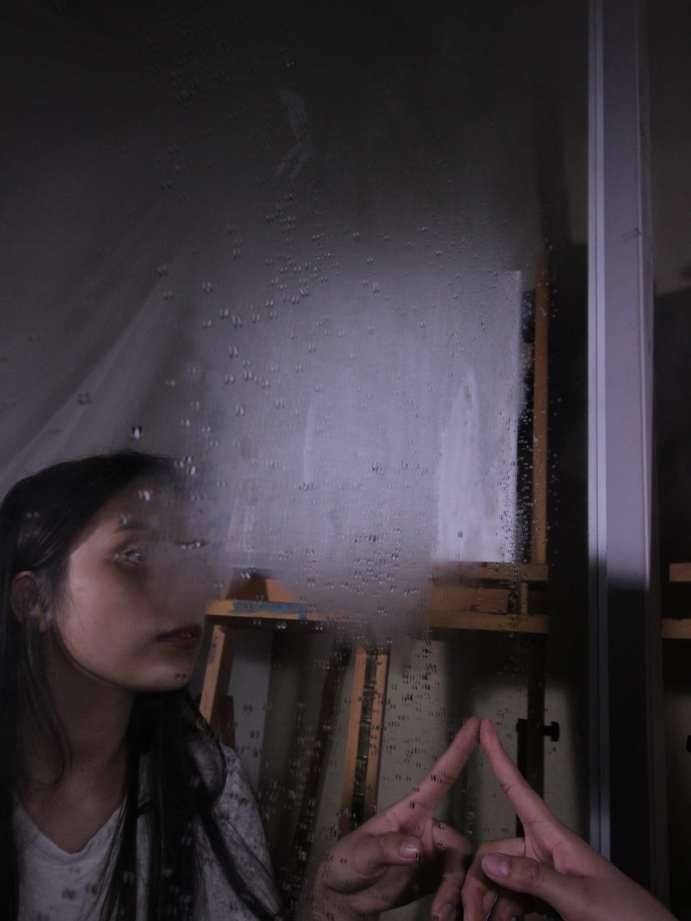 Girl with hand out in front of a mirror with fog covering her reflection.