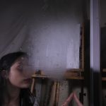 Girl with hand out in front of a mirror with fog covering her reflection.