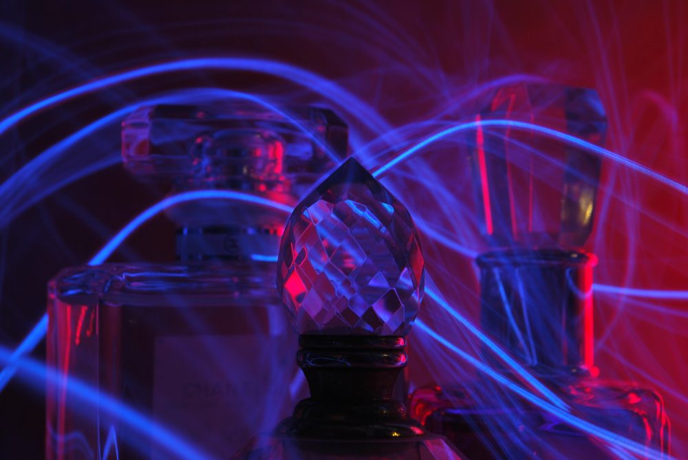 Three glass perfume bottles sitting next to each other with a rope of light intertwining them.