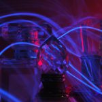 Three glass perfume bottles sitting next to each other with a rope of light intertwining them.