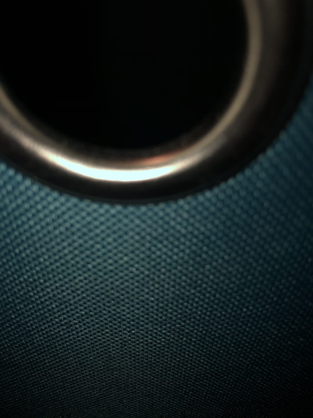 A metallic silver ring connected to a blue tarp texture, all set against a foreground and background of darkness.