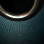 A metallic silver ring connected to a blue tarp texture, all set against a foreground and background of darkness.