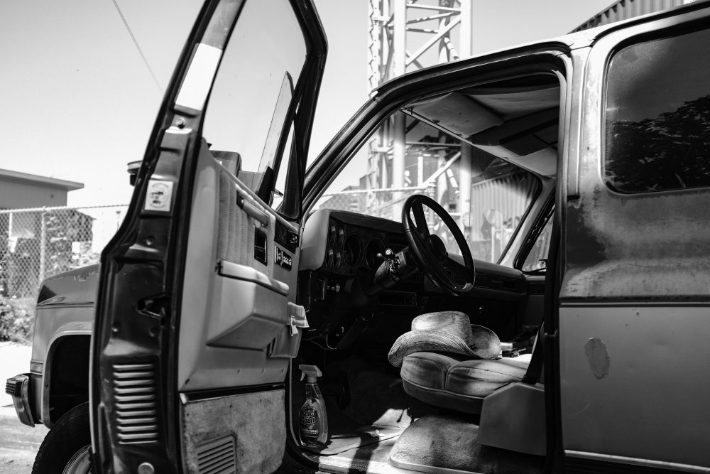 This is a black and white image of the open front door of a pickup truck. Inside the truck, you can see a straw cowboy hat on the driver's seat.