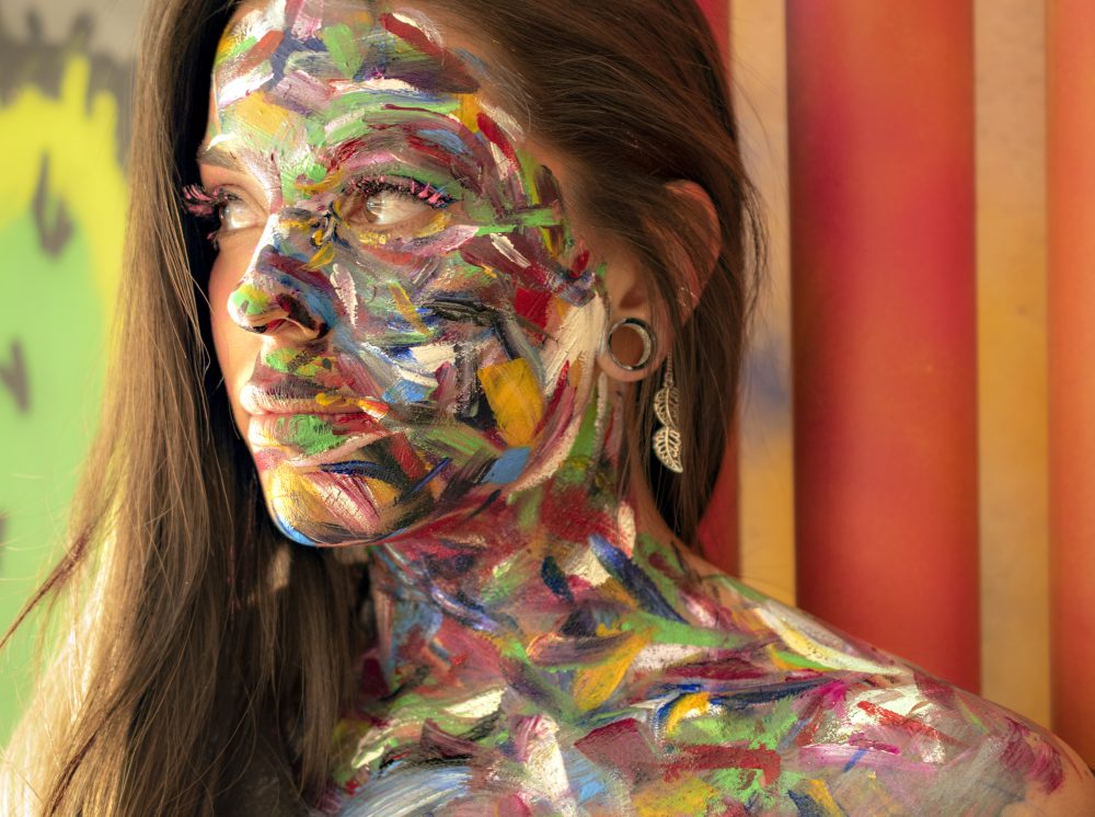 Photo of a female model with a bright vibrant background, and paint all over her body.