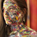 Photo of a female model with a bright vibrant background, and paint all over her body.