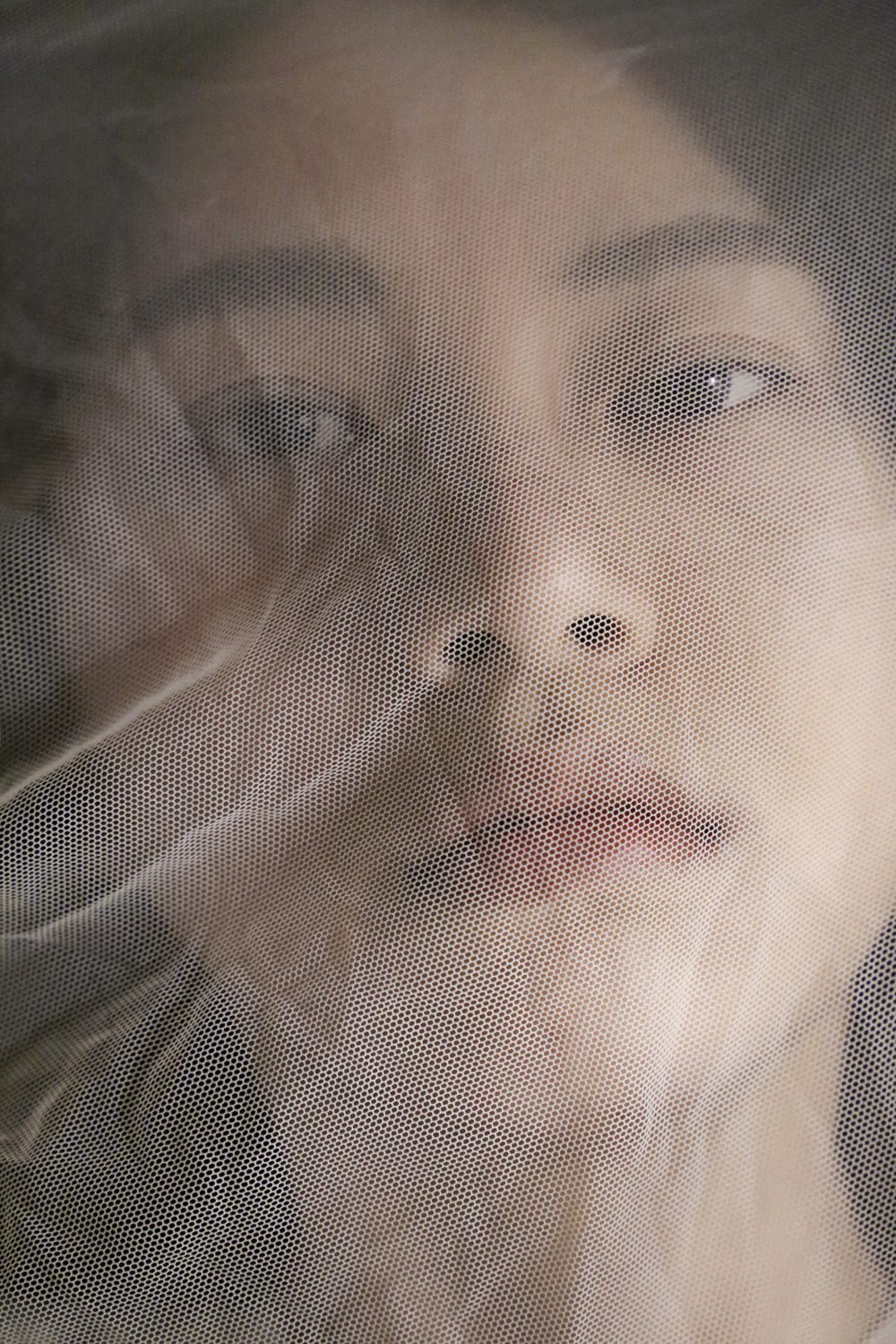 Photograph of a woman looking at the camera with a thin layer of white cloth in front of her face.