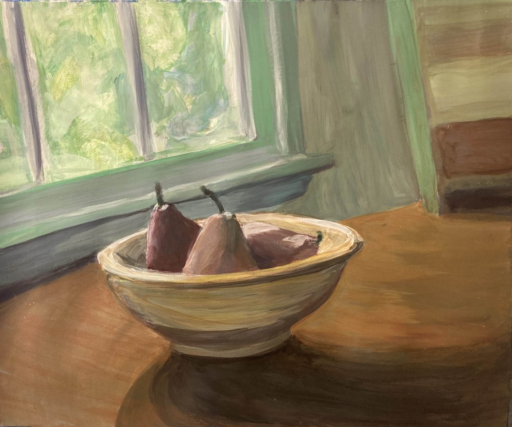 Three red Bartlett pears resting in a ceramic bowl on a wooden countertop, in front of a window, with sun filtering through the leaves of the trees outside.