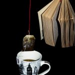 A book held up in empty space with bright red string, next to a cup of tea and teabag being held up by bright red string as well