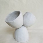 Three cups stacked: one at the base is upside down, while two are balanced atop it face-up