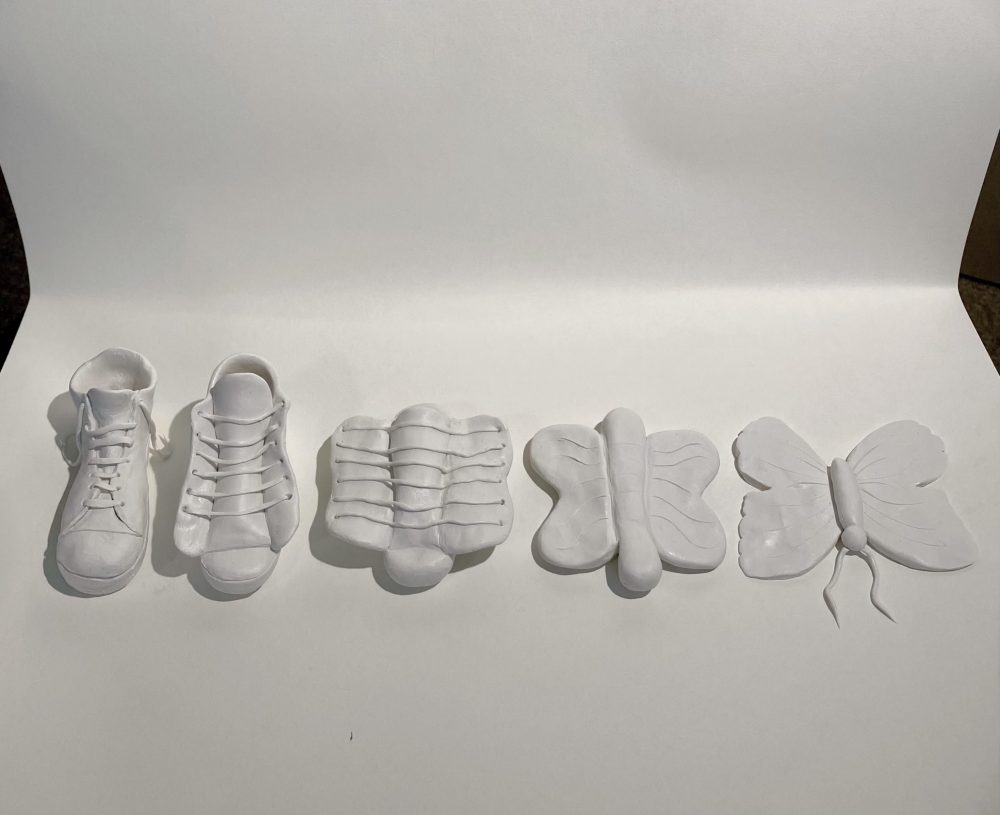 A polymer clay project in white of a shoe pair transforms to a butterfly.