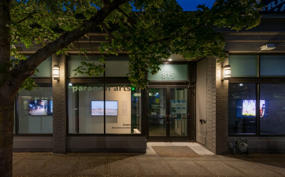 Window view of Paragon with three monitors playing videos at night.