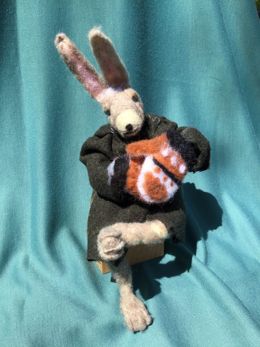 This is a bunny figure made of wool felt sitting down with mittens and a jacket.
