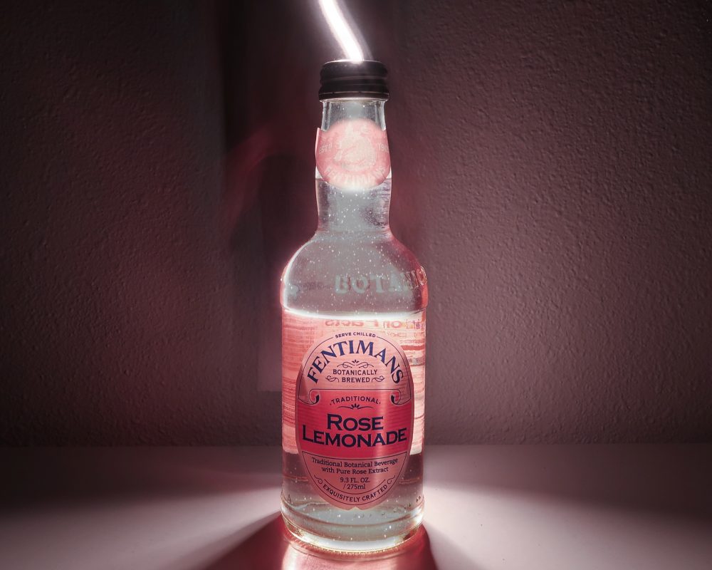 A photograph of a glass bottle with a pink background.