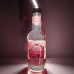A photograph of a glass bottle with a pink background.