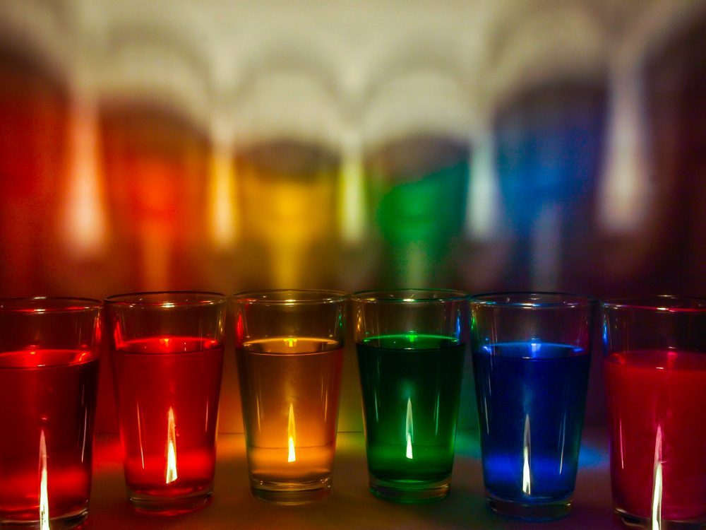 Photograph of small glasses with liquid in rainbow colors inside each glass.