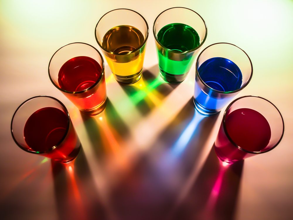 An aerial view of a semi-circle of cups with water in them. The water is rainbow colored.