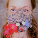 A 3D design of a lower half of the face mask, covered in rocks and decorated with live flowers.