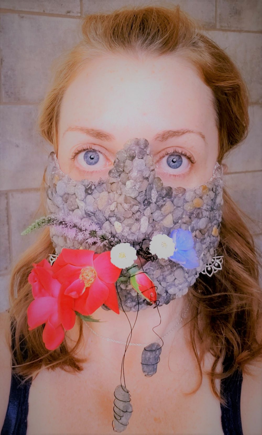 A 3D design of a lower half of the face mask, covered in rocks and decorated with live flowers.