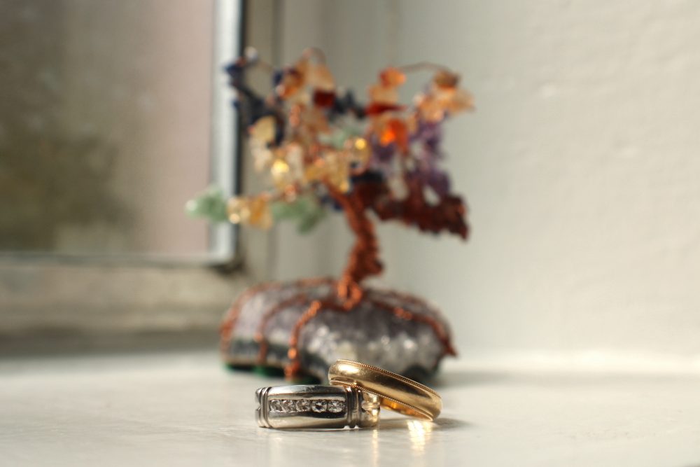 Image of two rings in front of a handmade tree of copper wire and colorful gemstones.