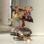 Image of two rings in front of a handmade tree of copper wire and colorful gemstones.