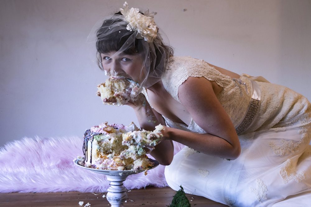 Person in a wedding dress eating cake with their hands.