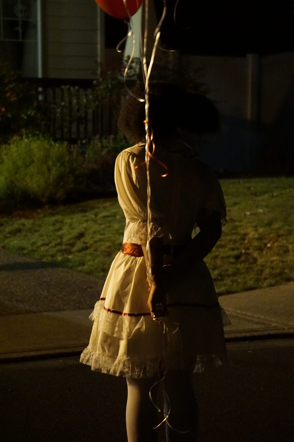 Girl from behind, holding red balloons in a white lace dress, staring into the distance.