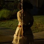Girl from behind, holding red balloons in a white lace dress, staring into the distance.