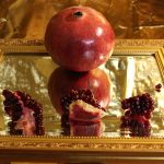 A photograph of a whole pomegranate and three pomegranate pieces served onto a mirror with a gold background.