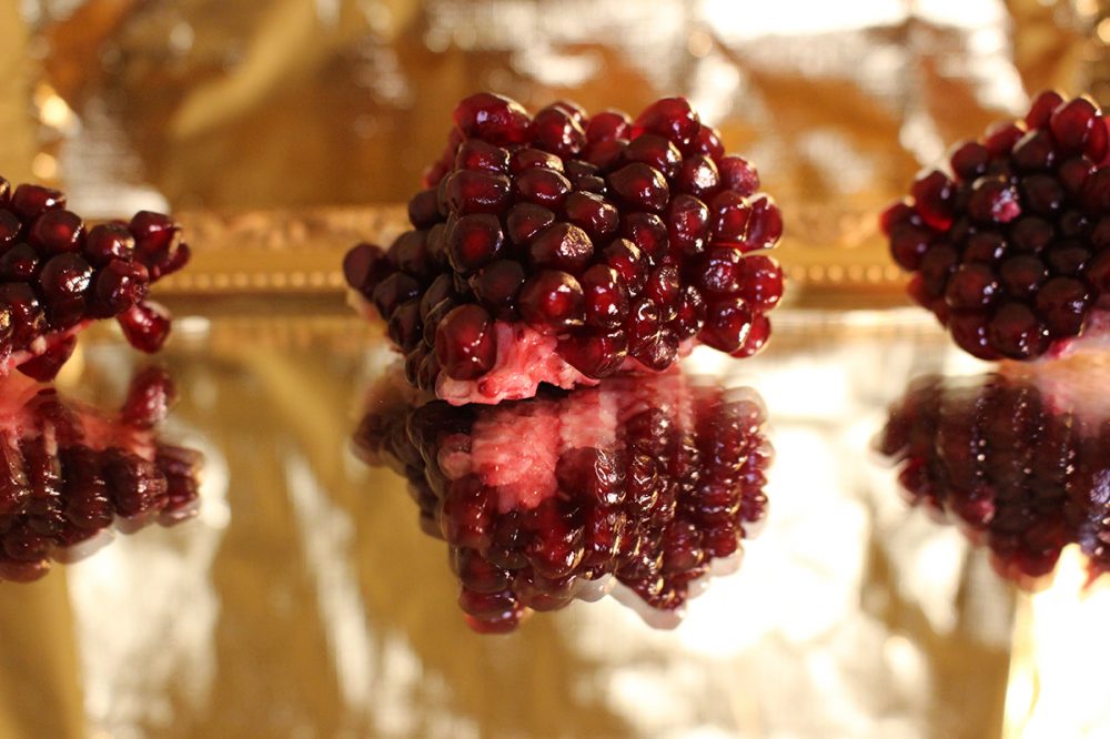 Pomegranate pieces and seeds on a mirror with a golden background.