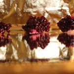 Close up of pomegranate pieces and seeds on a mirror with a gold background.