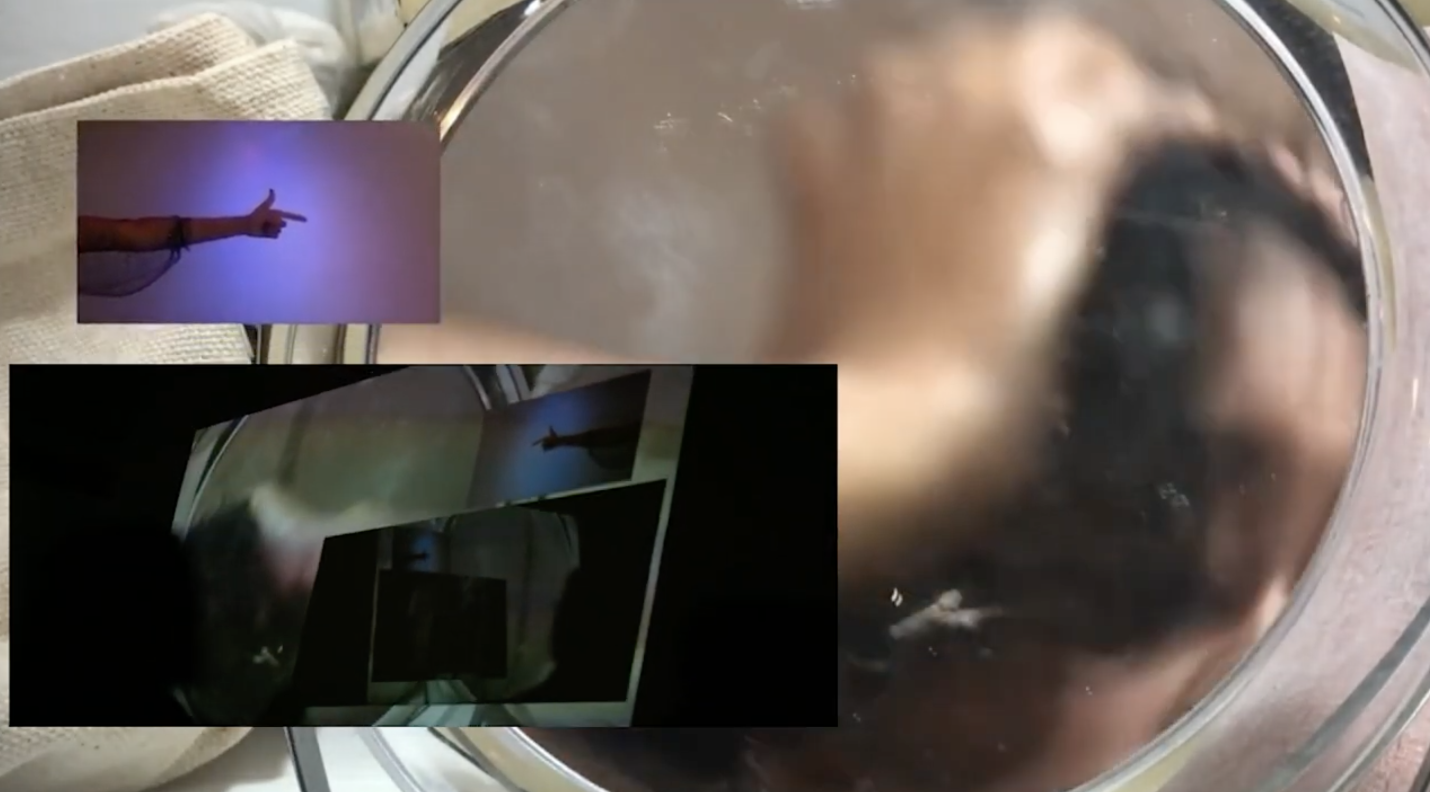 A video still of a hand mirror layered with two other video images of lights and darks and an arm and hand pointing