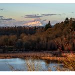 Landscape photograph of a lake of water with two mountains in the background separated by a large amount of space, with birds seen traveling through the scene.