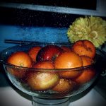 A photograph of water droplets being showered onto fruit for a nice cleaning. With a flower pot and a blue bread basket to show more vibrant colors.