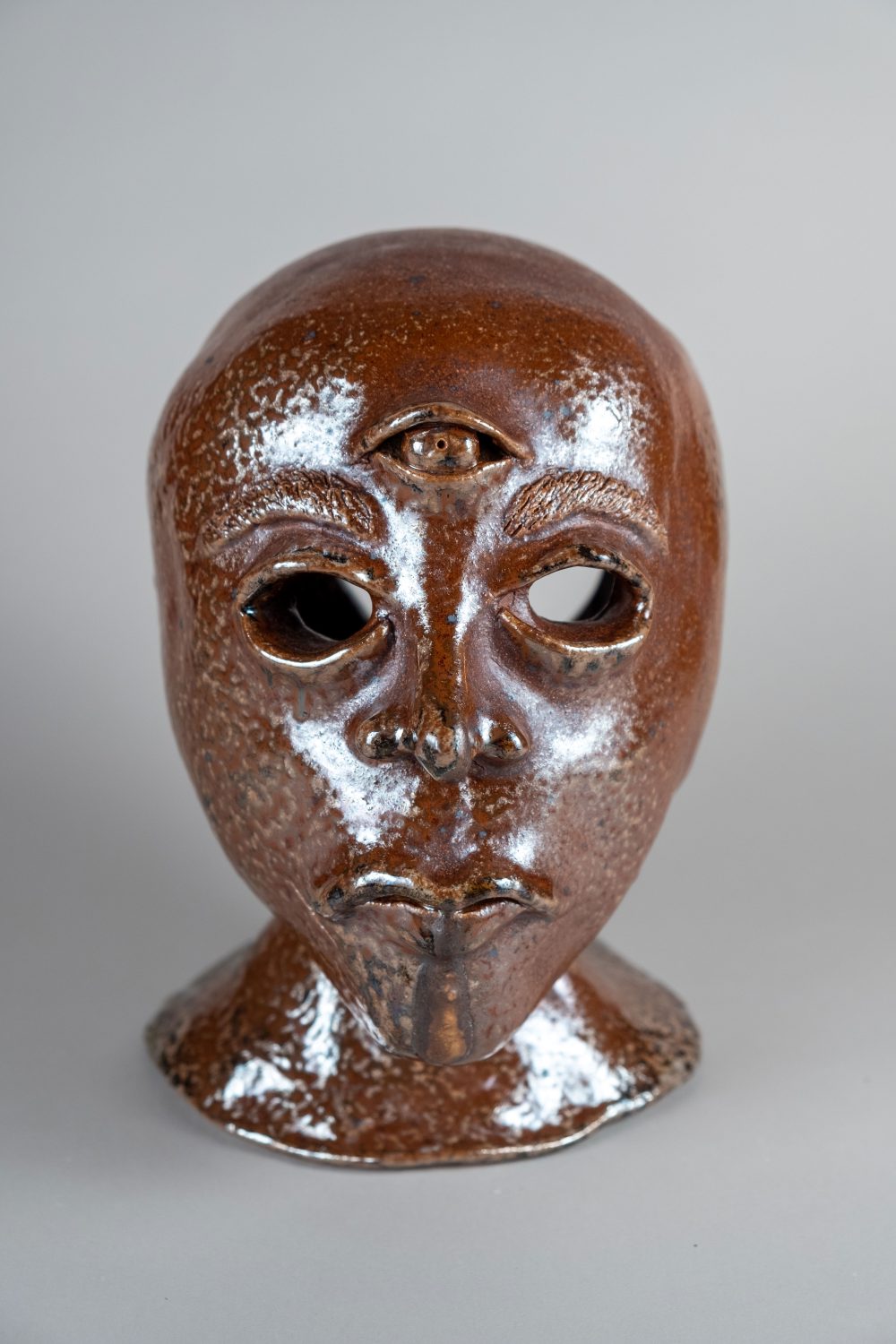 Ceramic sculpture of a human head with an all knowing third eye placed on the forehead.