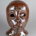 Ceramic sculpture of a human head with an all knowing third eye placed on the forehead.