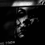 Black and white photograph of a commercial poster of a woman's face, partly covered by the shadow of a tree branch.