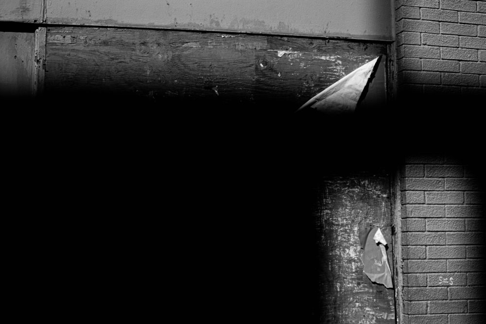 Shadow cast upon an industrial plywood wall tattered with torn paper and degraded paint.
