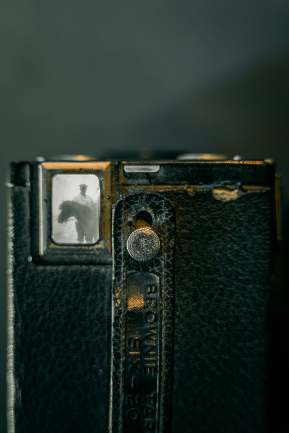 Color photo looking through the viewfinder of a Kodak Brownie at an old black and white photograph of a man standing behind a horse.