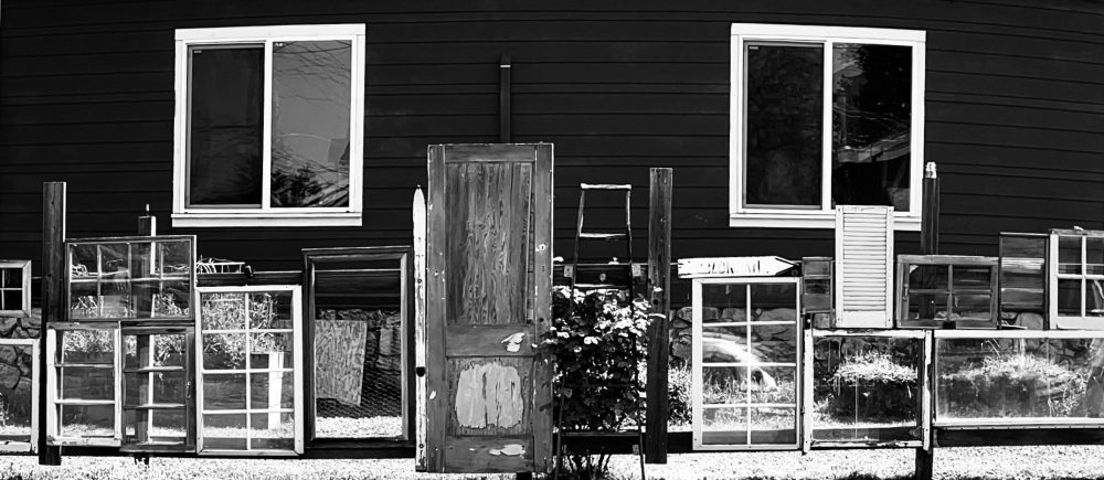 Black and white photo of a fence made with windows and a door.